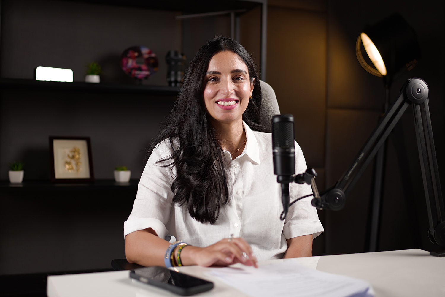 Photo of a person in a podcast recording studio smiling and looking at the camera