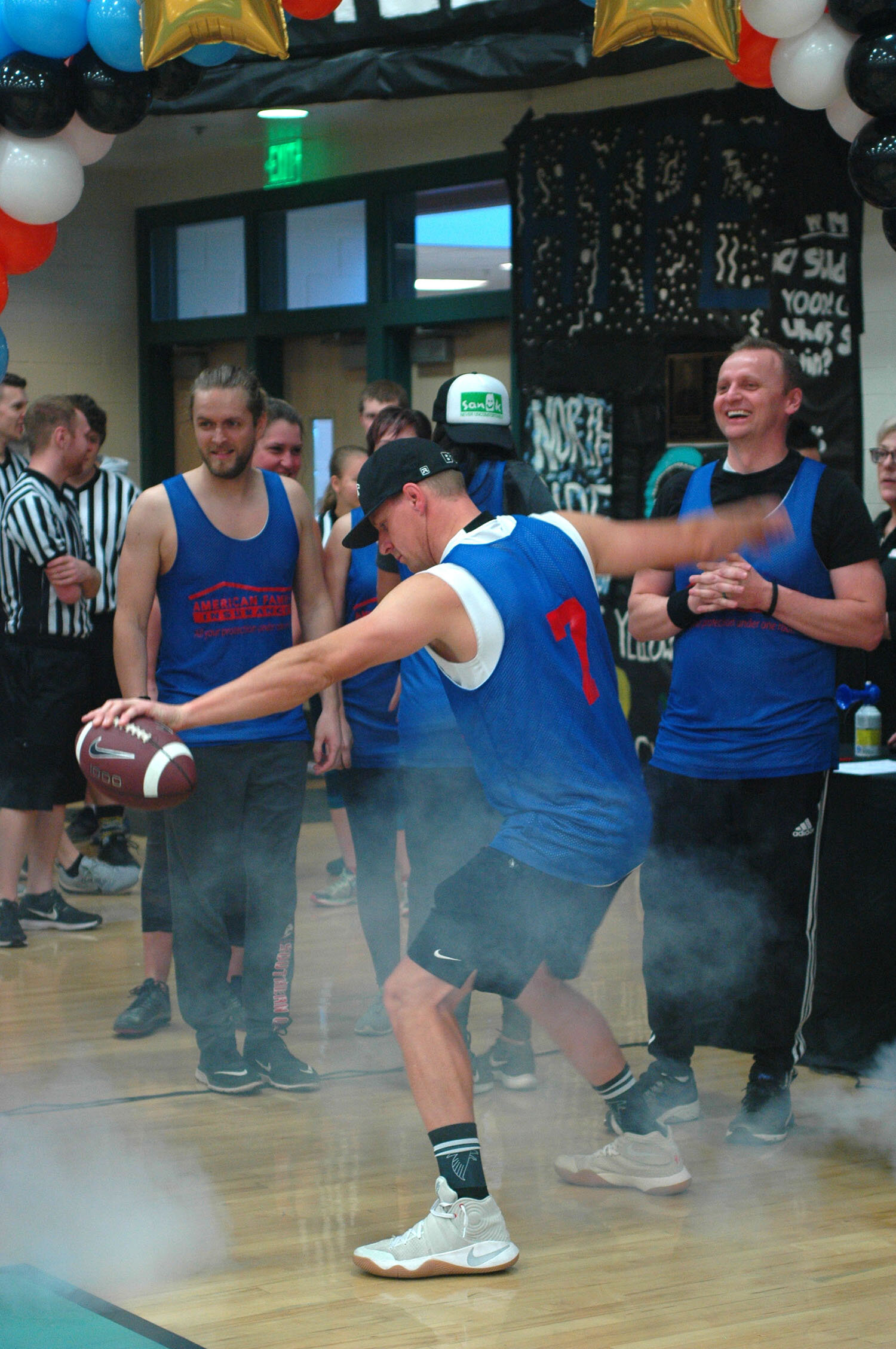 Man wearing a blue tanktop, shorts, and baseball cap dancing with fog around him in a gymnasium