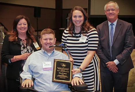 Brian Denny (second from left), accompanied by his wife Jessica, receives the 2016 Client Achievement Award from Dr. Roxzanne Breland, Chair of the SC State Agency of Vocational Rehabilitation, and Neal Getsinger (right), VR Commissioner.