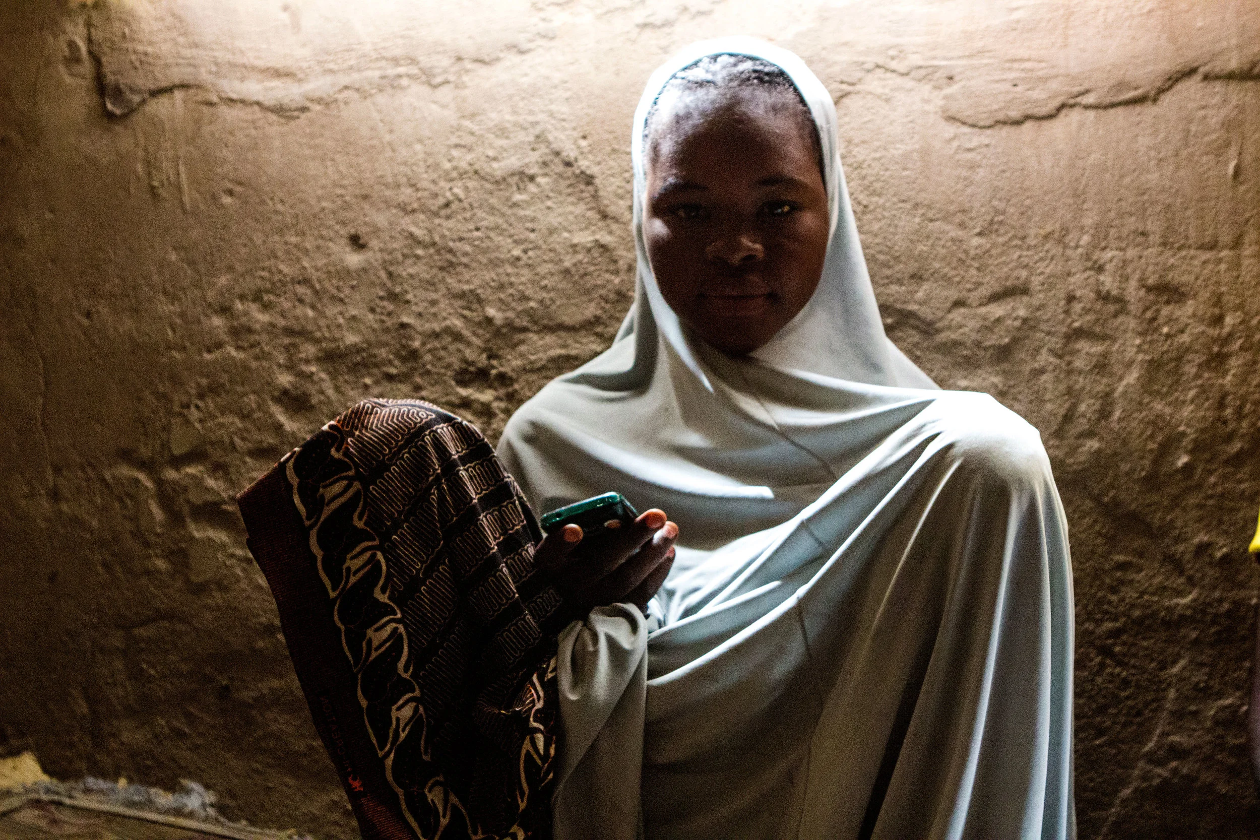 Yola, Nigeria. March 6 2015. Aisha, 17, poses for a photo after sending SMS messages on her cell phone. She sits in the one-room house her family now rents after fleeing Boko Haram violence in her hometown.