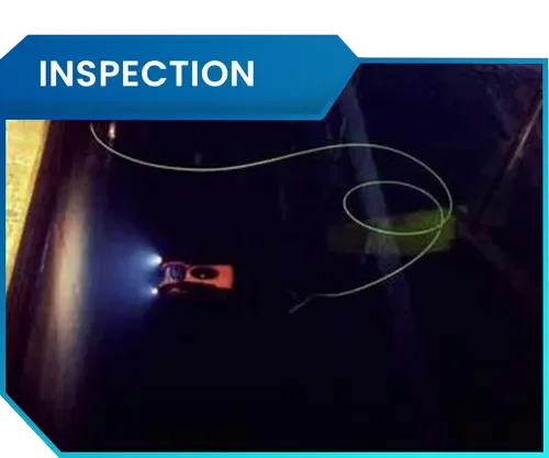 Inspection of a dark surface with a flashlight and a small orange device, revealing some wires or strings on the surface.