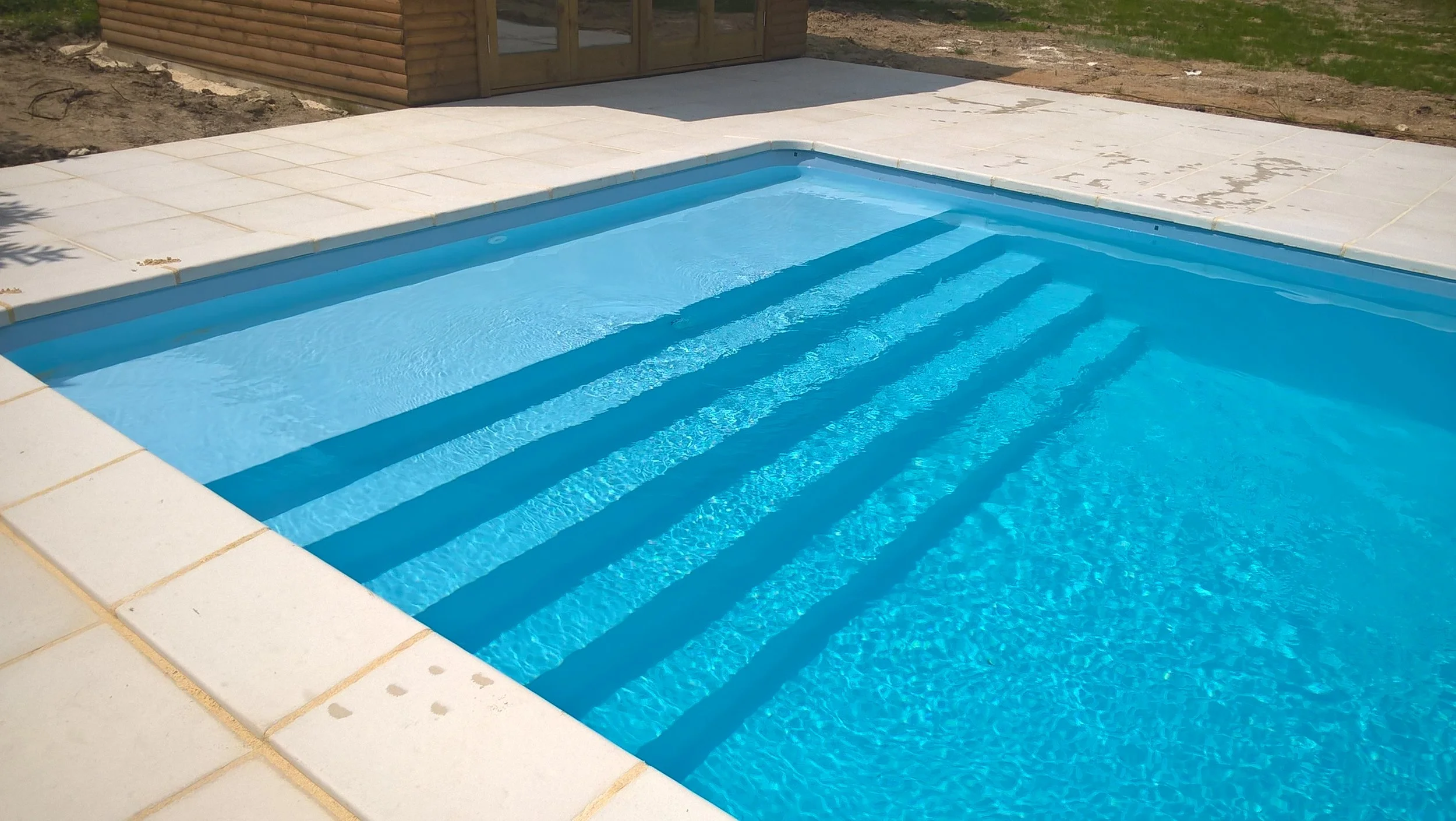 9 m by 4 m in-ground pool with full width steps, clear blue liner and stone terrace.