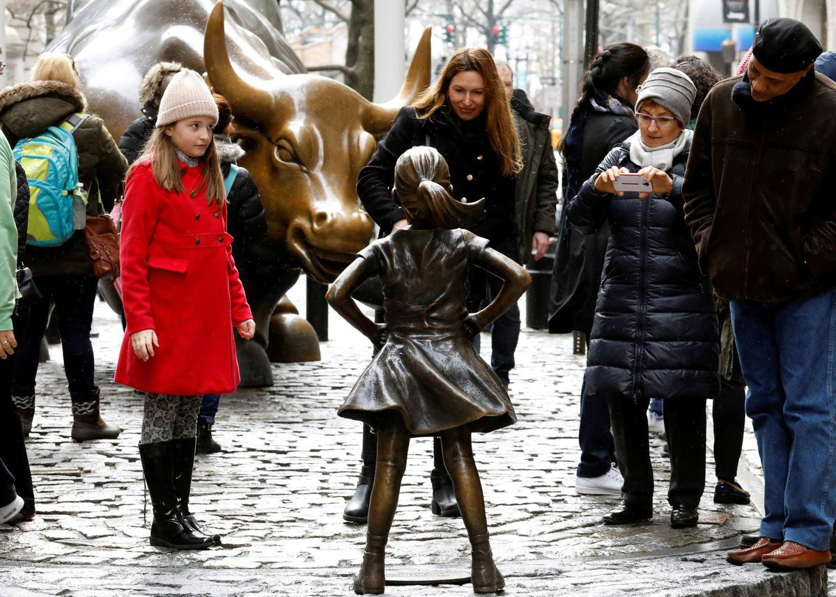 People look at a statue of a girl facing the Wall St. Bull, as part of a campaign by U.S. fund manager State Street to push companies to put women on their boards, in the financial district in New York, U.S., March 7, 2017. BRENDAN MCDERMID/REUTERS