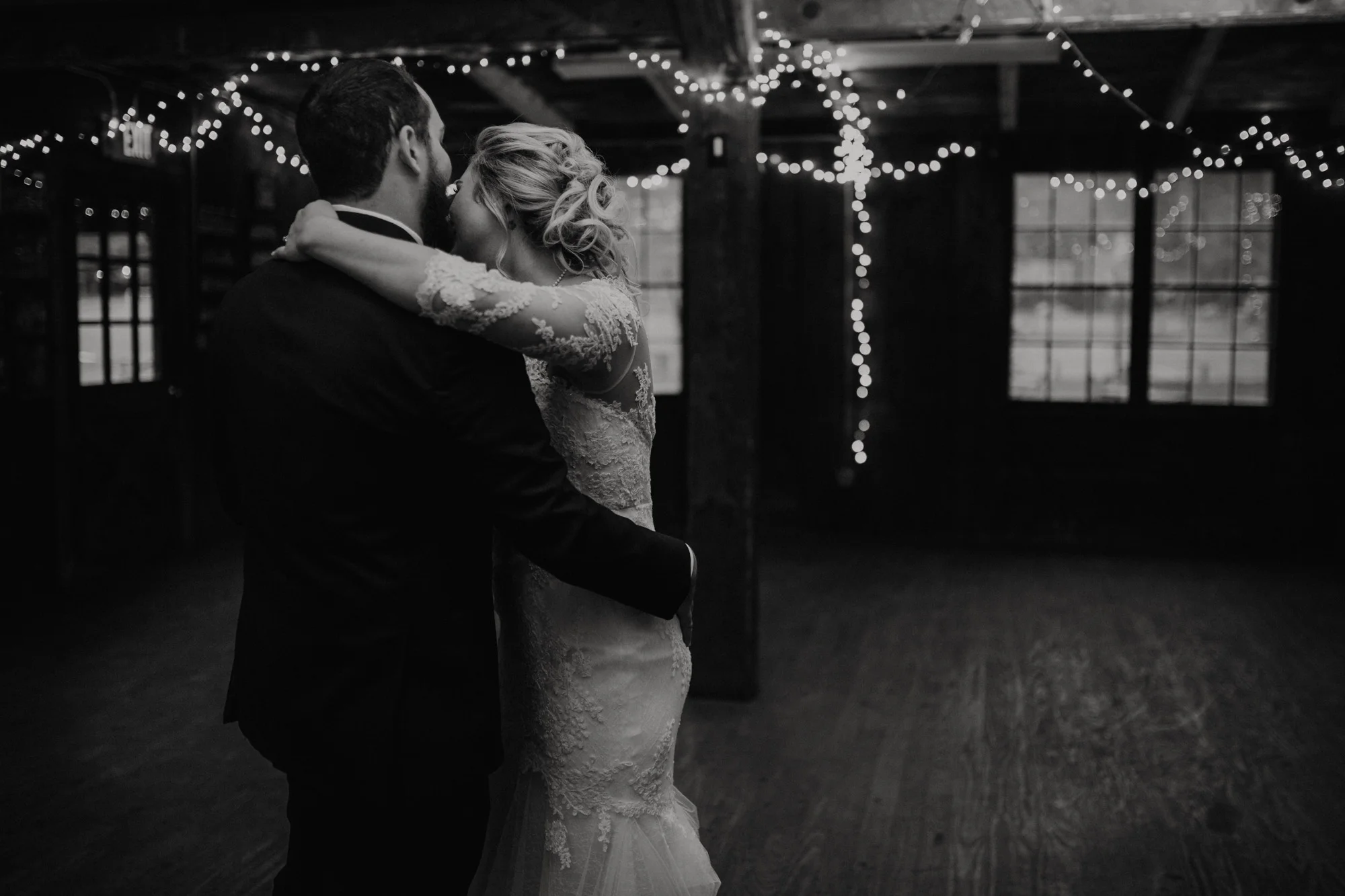 The bride and groom have their first dance beneath fairy lights in the camp’s mess hall