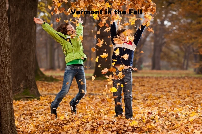 Two children playing and throwing autumn leaves in a park with trees in fall colors, with the text 'Vermont in the Fall' at the top.