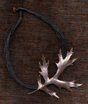 A necklace with a silver deer antler pendant on a black cord, placed on a wooden surface.
