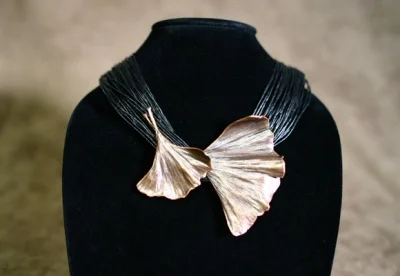 Necklace with pendant shaped like a ginkgo leaf on a black display bust.