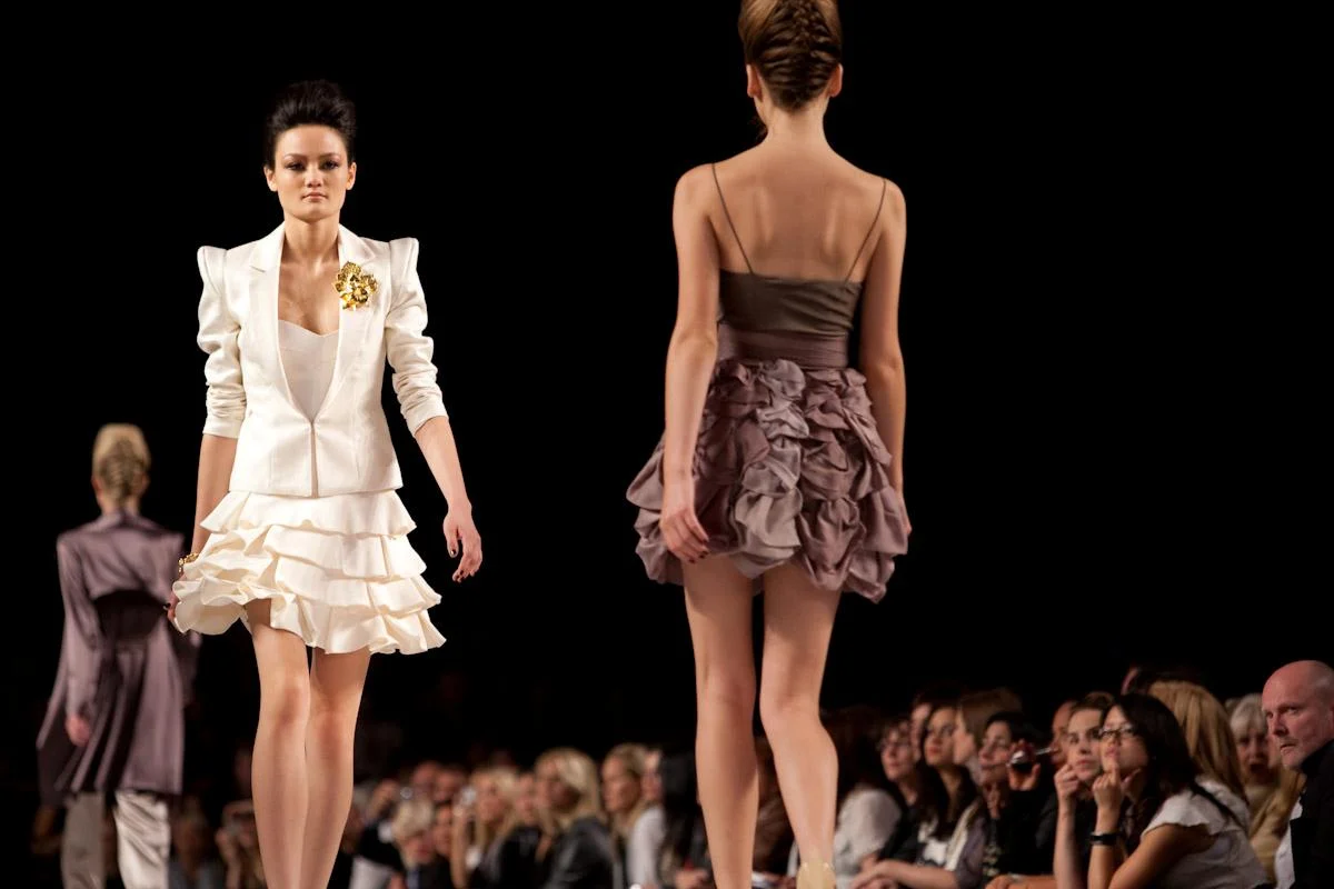 Models walking on runway at fashion show, with audience watching.