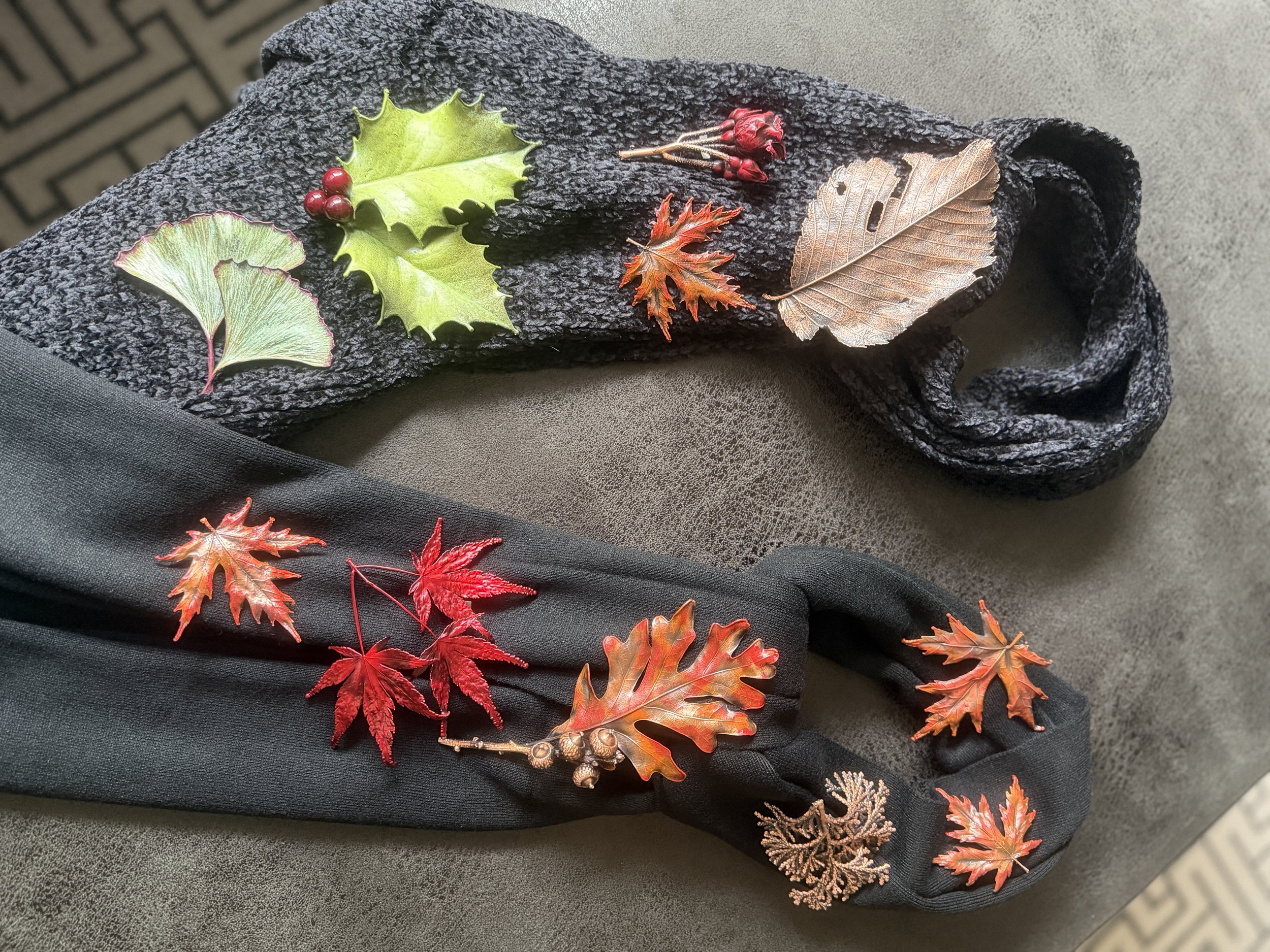 Arrangement of artificial autumn leaves, berries, and small decorative items on a black textured surface.