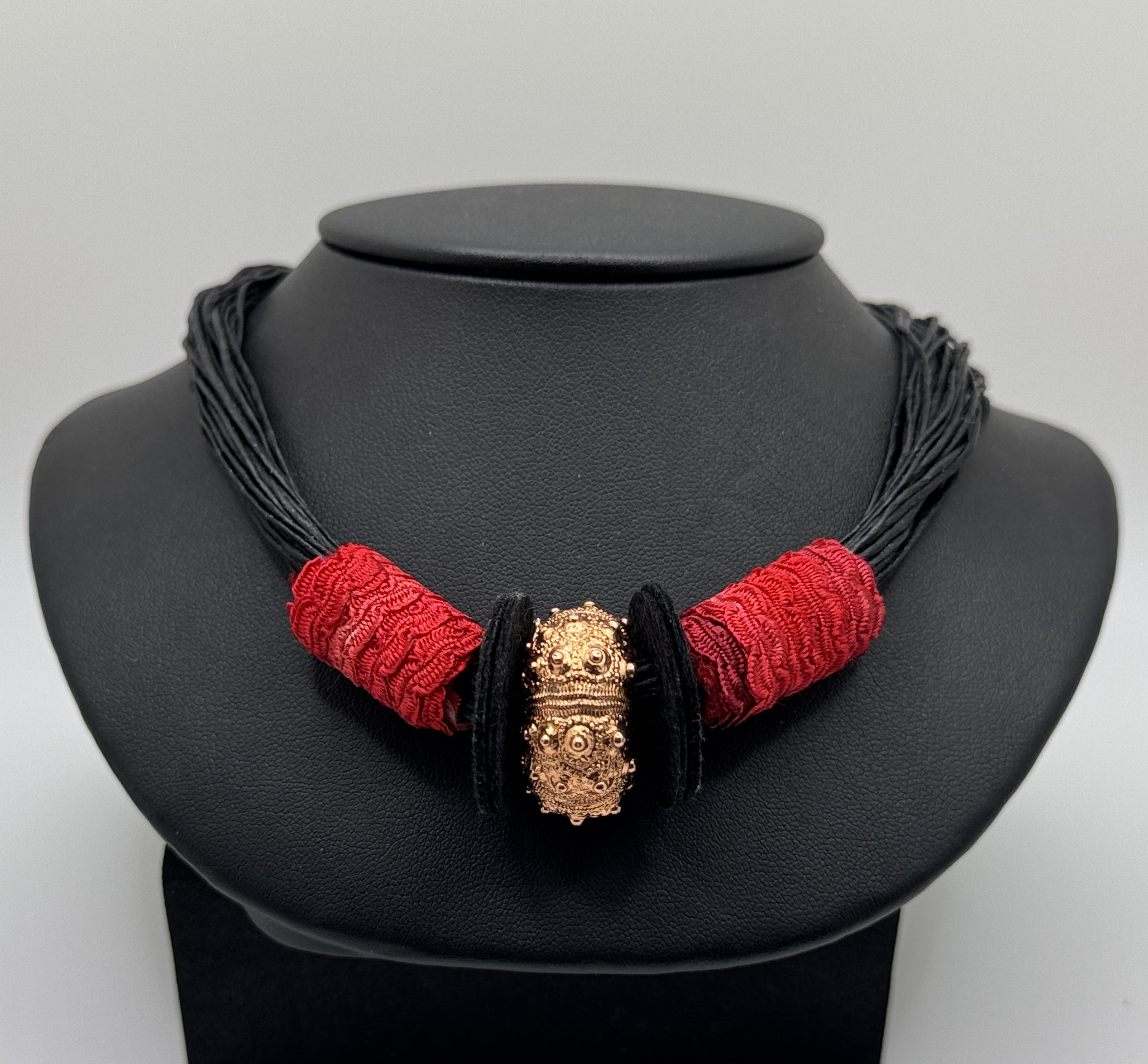 Black jewelry display bust featuring a layered black necklace with red and gold decorative beads.