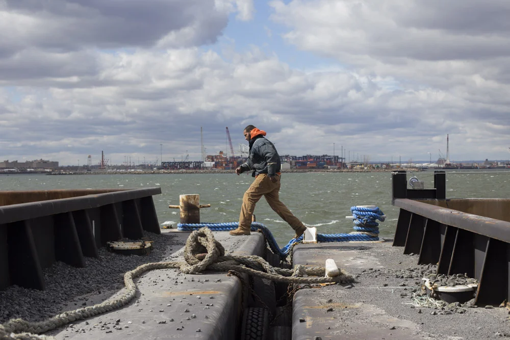 Walter Serrano, a tugboat deckhand for Brown and Sons towing, crosses between barges while moving cargo in a small inlet by Red Hook. 
