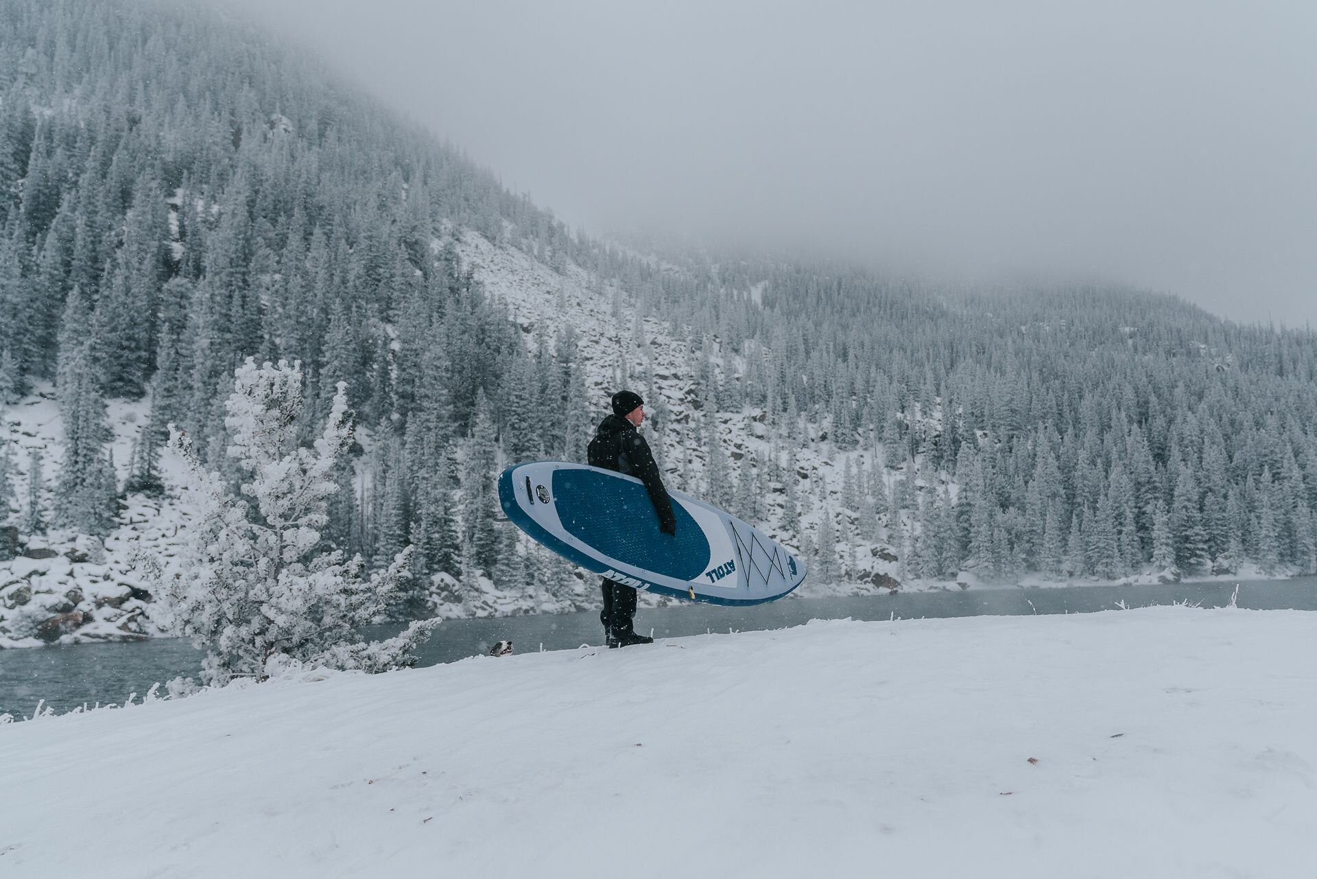 A man with his Atoll inflatable paddle board near a cold water during winter