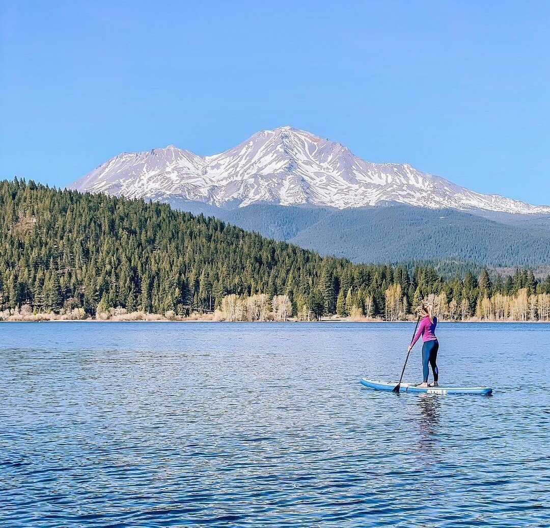 A lady paddling an inflatable paddle board on a lake near Mt. Sasha