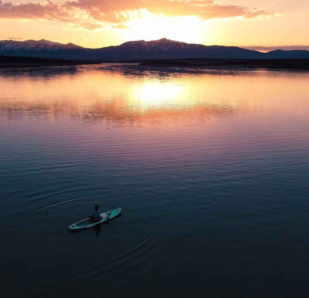 person sitting on an inflatable paddle board in a lake during sunset