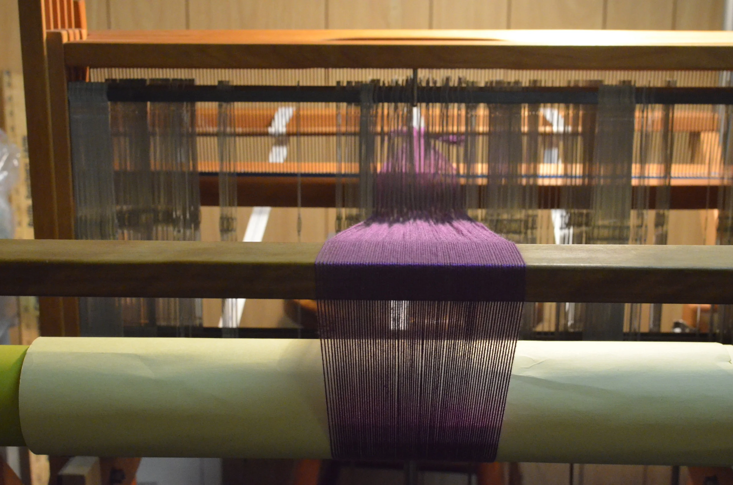 4) The most complicated part of the process (...besides possibly the calculations...) is warping (or dressing) the loom. Each thread must be carefully pulled through the beater (seen below) and a heddle (those vertical metal things in this picture), arranged specifically for the desired pattern. Once the warp is fastened to the back of the loom, an intricate process is used to roll up the warp, making sure tension is kept steady and even. The front is tied off and we're ready to begin!