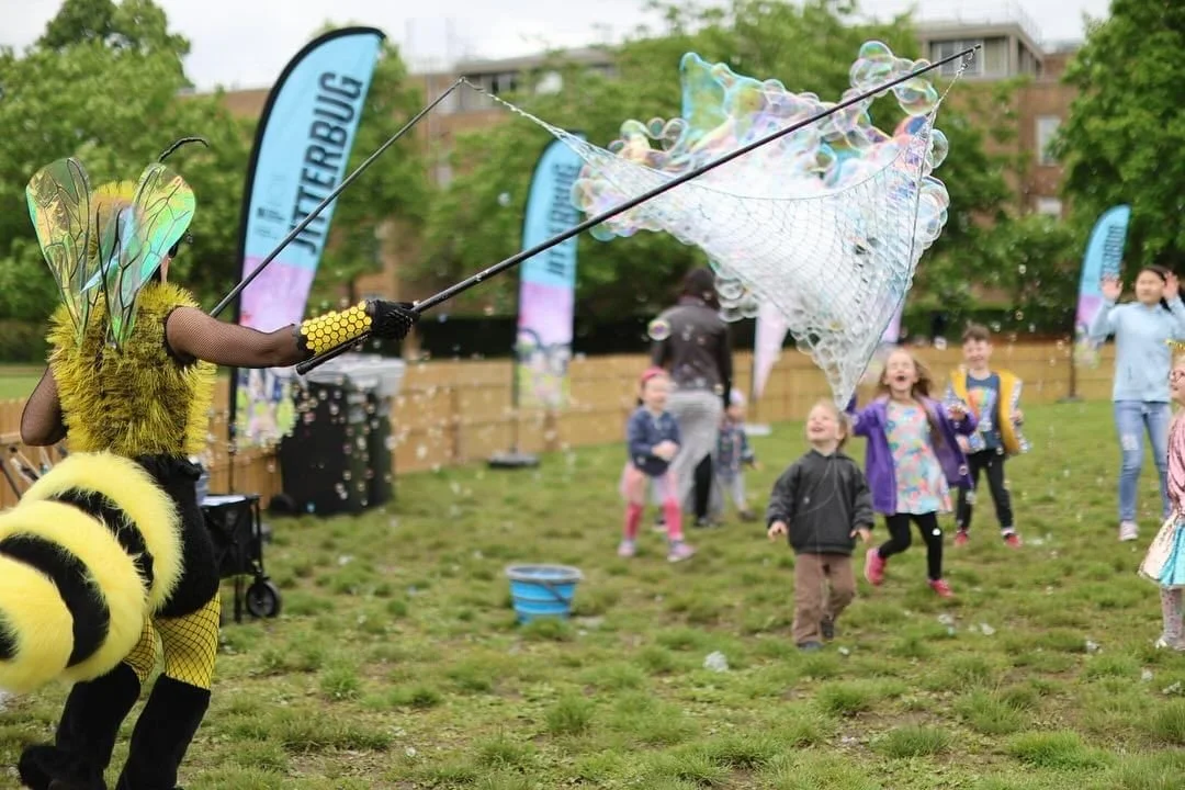 A person dressed as a bee blowing bubbles for children in a park.