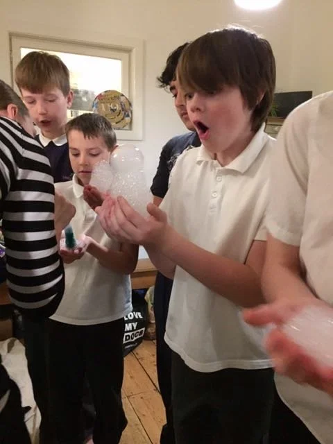 Group of boys gathered indoors, with one boy holding soap foam and expressing surprise.