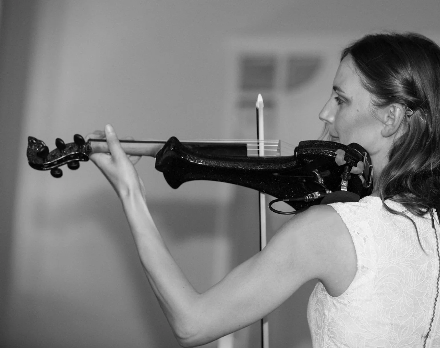 A woman playing a violin, focusing intently on her performance, with a music stand in front of her, photographed in black and white.