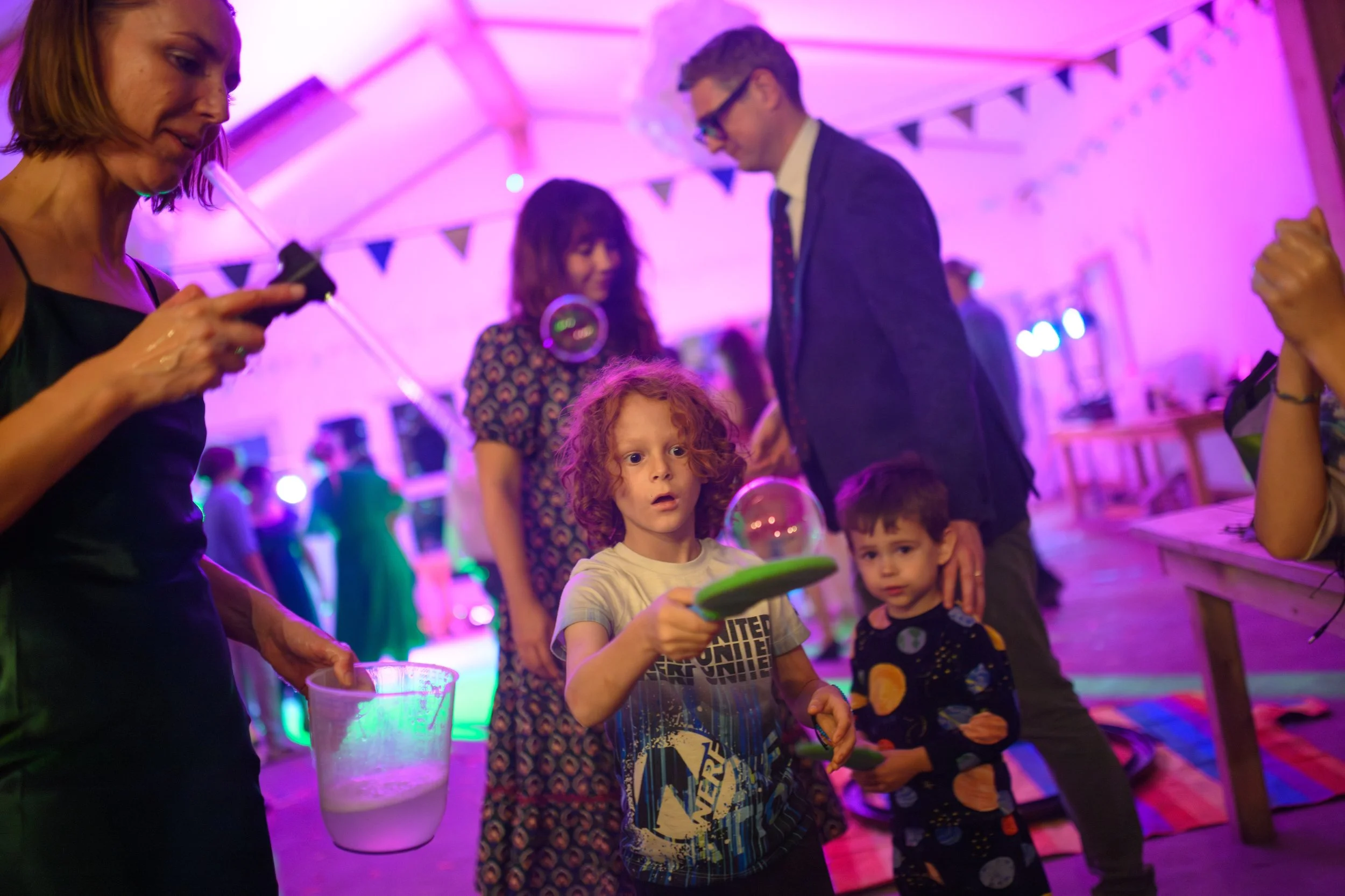Children playing with bubbles at a party with colorful lighting and decorations.