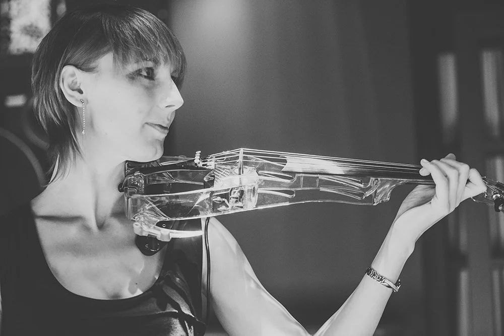A woman playing a transparent electric violin indoors.