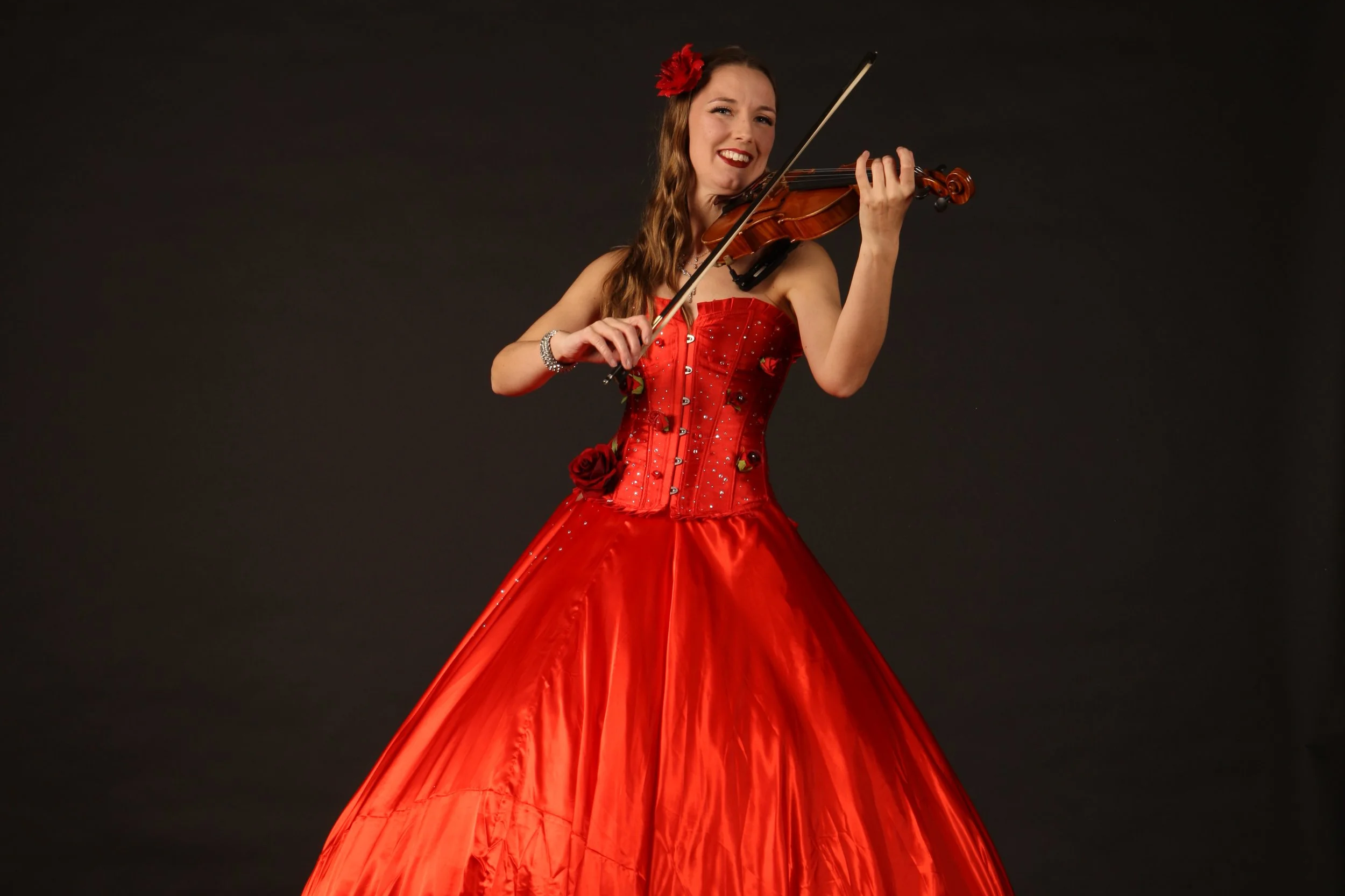 Woman on stilts dressed in red flamenco-style dress playing the violin against a dark background.