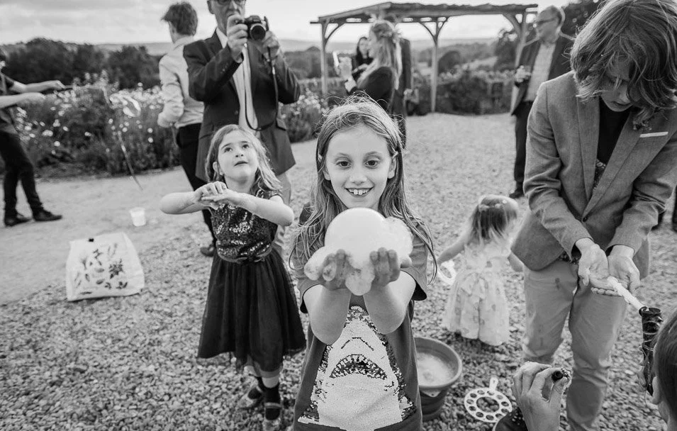 Children and adults at an outdoor celebration, with a girl holding a large cotton candy, others playing and taking photos.