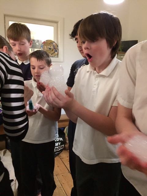 Group of boys in a room with one holding a handful of soap bubbles, surprised and excited.