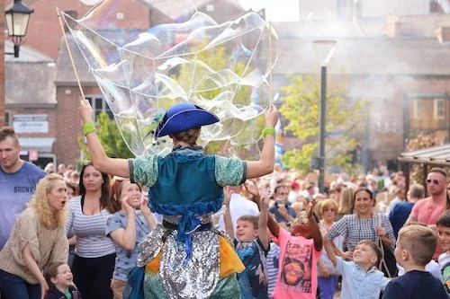 Performer creating large soap bubbles in front of a crowd in an outdoor setting.