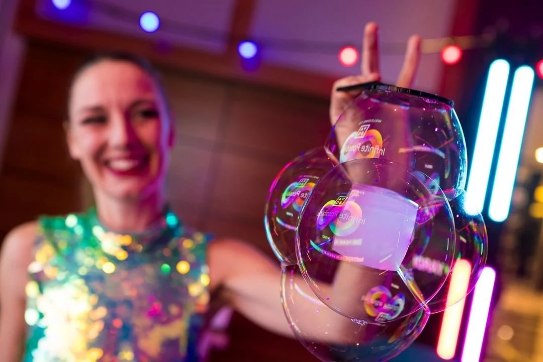 A woman smiling at a party, holding a bubble cube close to the camera, with colorful neon lights in the background.