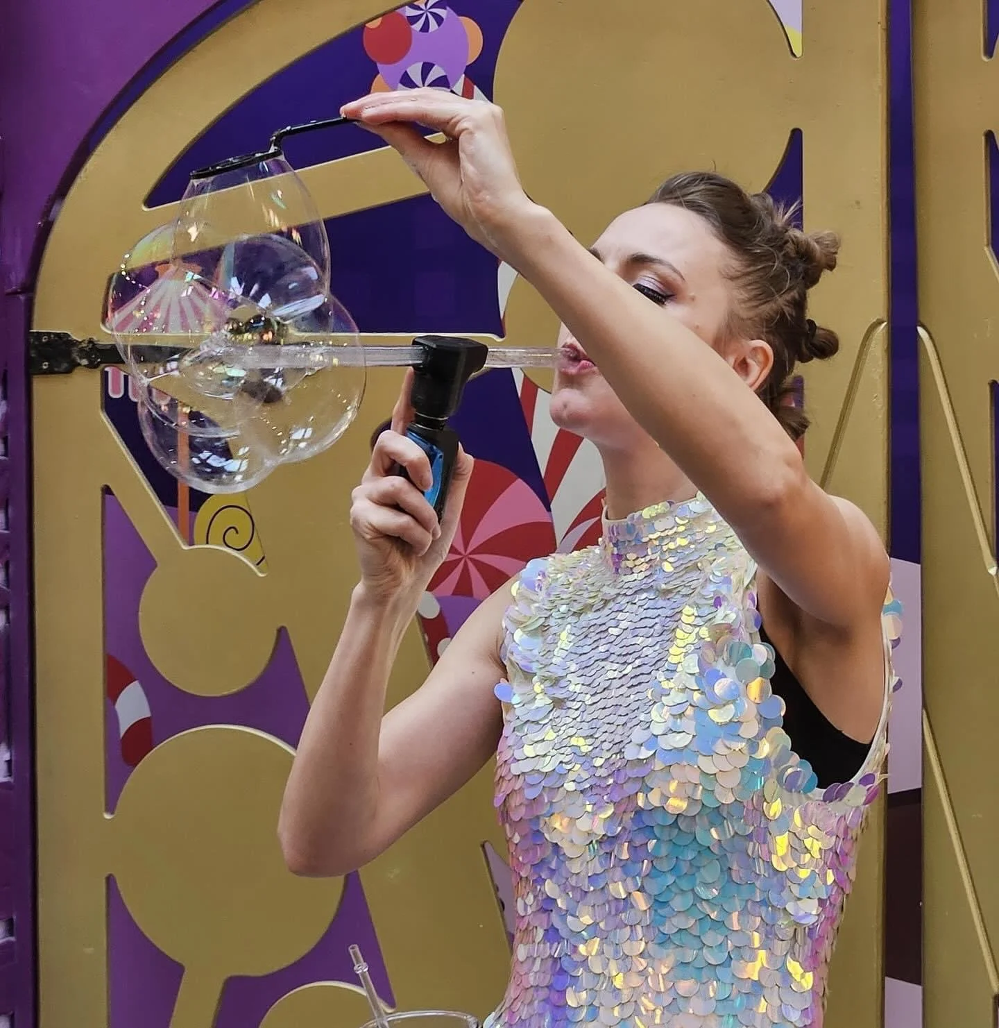 A woman in a shimmering, iridescent dress blowing bubbles with a bubble wand.