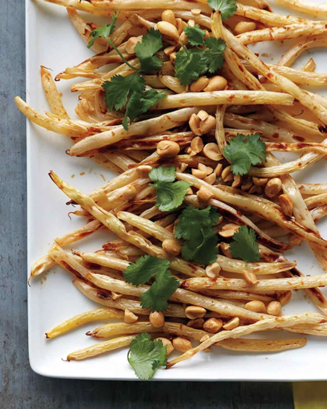 Ingredients 1 pound wax beans, trimmed 1 tablespoon olive oil Coarse salt and ground pepper 2 teaspoons soy sauce 1/4 teaspoon finely grated peeled fresh ginger 3/4 teaspoon fresh lemon juice 1/2 teaspoon light-brown sugar 1/4 cup unsalted peanuts 1/4 cup fresh cilantro leaves Directions Preheat oven to 450 degrees. On a rimmed baking sheet, toss wax beans with oil and season with salt and pepper. Roast until browned in spots and tender, about 15 minutes, tossing halfway through. In a medium bowl, combine soy sauce, ginger, lemon juice, and sugar. Add roasted beans, peanuts, and cilantro and toss to combine. Adapted from Martha Stewart, Everyday Food, July/August 2010