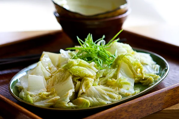 Stir Fried Chinese Napa Cabbage by steamykitchen on July 24, 2009 in Special Dietary Needs , Vegetarian Prep: 2 mins Cook: 5 mins Serves: 4 Ingredients 1 pound Napa Cabbage 1 Tablespoon Cooking Oil 1 teaspoon Freshly Grated Ginger 1 clove Garlic, Finely Minced 2 teaspoons Soy Sauce (lite) ¼ cups Broth Or Water 1 pinch Sugar 1 teaspoon Sesame Oil Preparation 1. Cut the napa cabbage into 1 1/2″ wide strips. Discard the end of the stem. Keep the thicker stems on one side of the cutting board, and the thin leafy leaves on the other side. 2. Heat a wok or large saute pan over medium-high heat. Add the cooking oil and when hot, add the ginger and the garlic. Cook for 15 seconds, until fragrant. 3. Add the thick napa cabbage stems, stir fry for 30 seconds. Pour in the soy sauce, broth (or water), and pinch of sugar. Add in the rest of the leafy leaves into the pan. Cover and cook for 2 minutes until cooked through. The thick stems should be still a bit crunchy, the leaves softened. 4. Drizzle with sesame oil and serve.