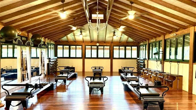 A Pilates or yoga studio with wooden floors, large windows, six Pilates reformer machines, and exercise balls on shelves. Pilates in Costa Rica. Pilates in Nosara.
