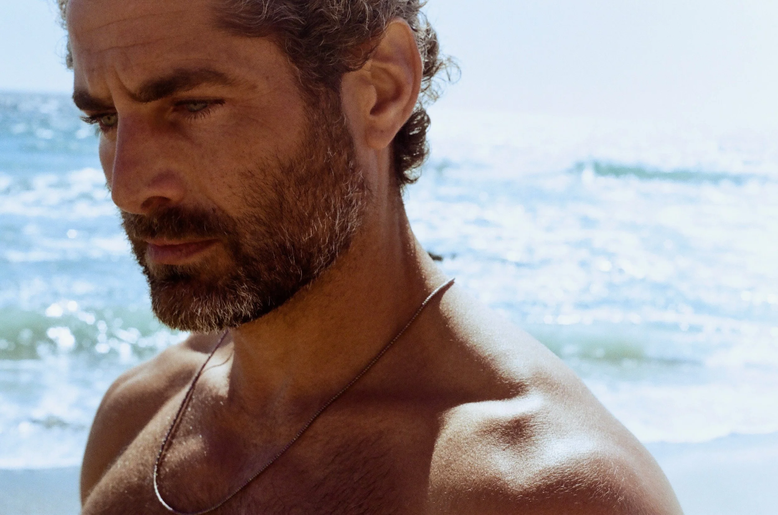 Close-up portrait of Nick Baga looking down, with the ocean behind him