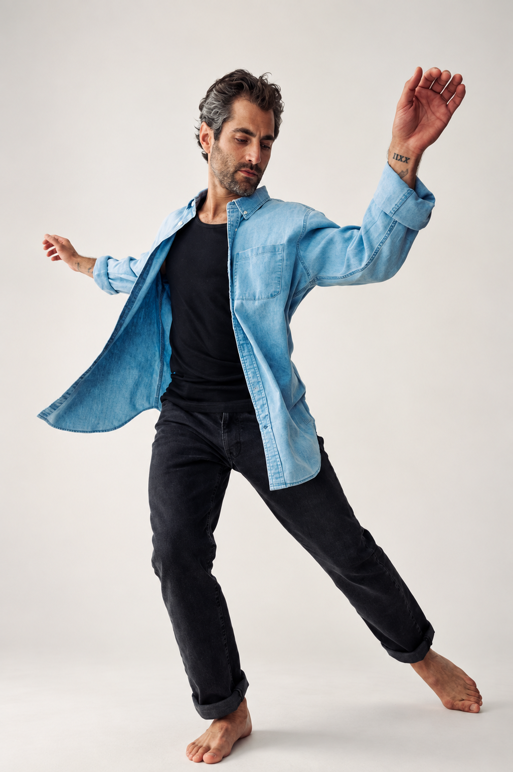 Nick Baga mid-movement in an open blue denim shirt and black pants against a white studio backdrop