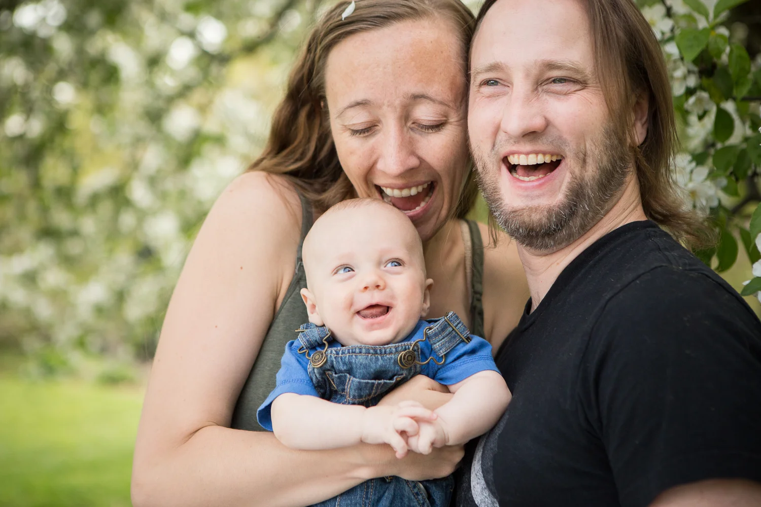 Laughing portrait of parents with baby boy under the spring flowering trees