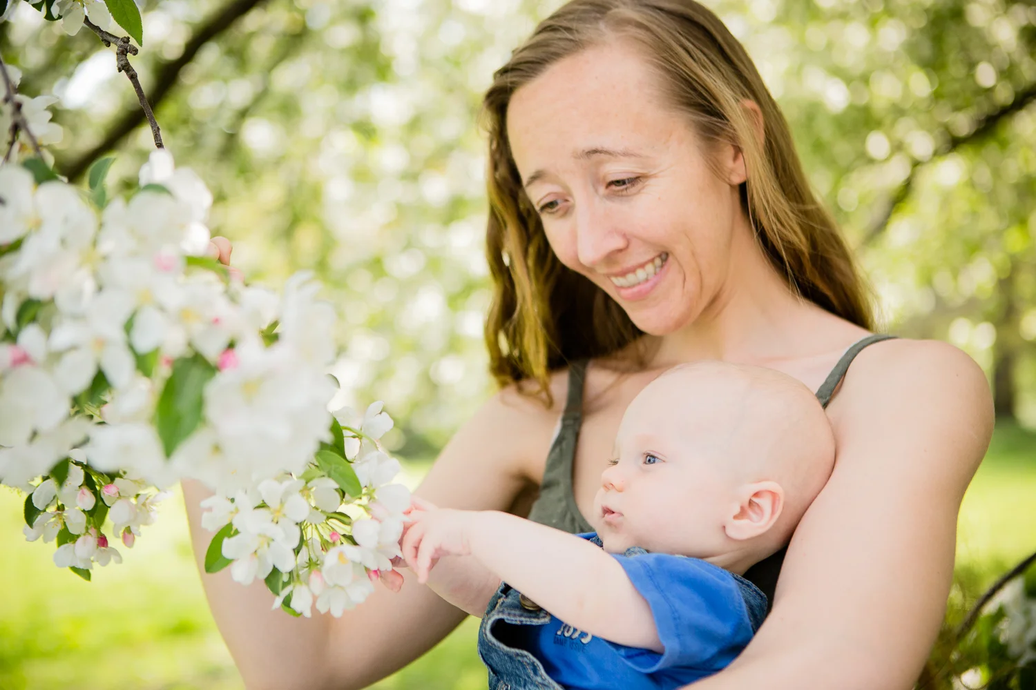 Mom holding baby boy and showing him the white spring blossoms