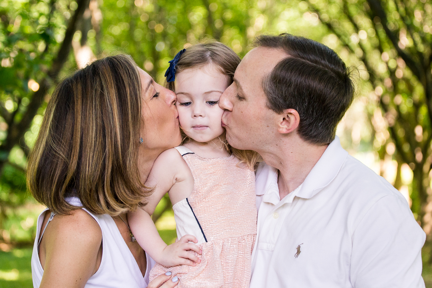 Portrait with attitude of mom and dad kissing their little girls cheeks at ...