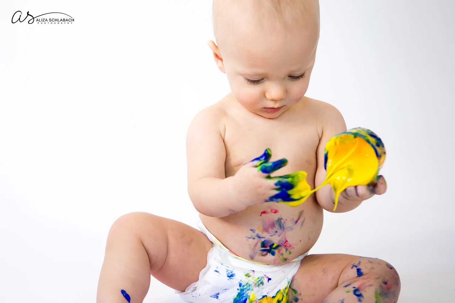 Photo of one year old naked baby boy about to spill fingerpaint
