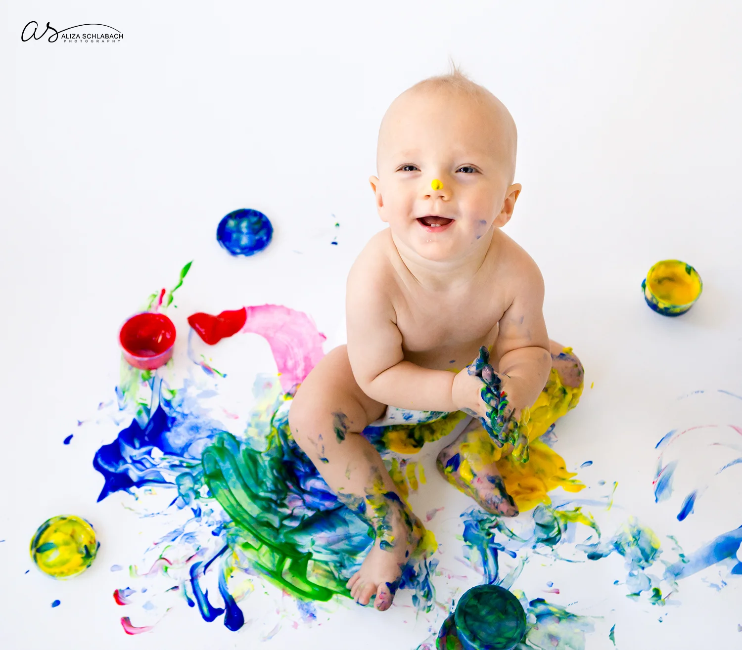 Photo of smiling one year old baby boy fingerpainting and lookup up at camera