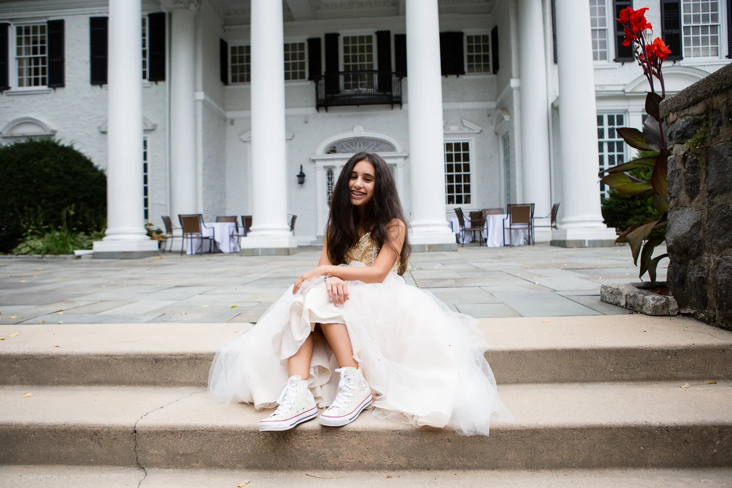 Photograph of Bat Mitzvah girl in white gown showing off her converse sneakers in front of country club