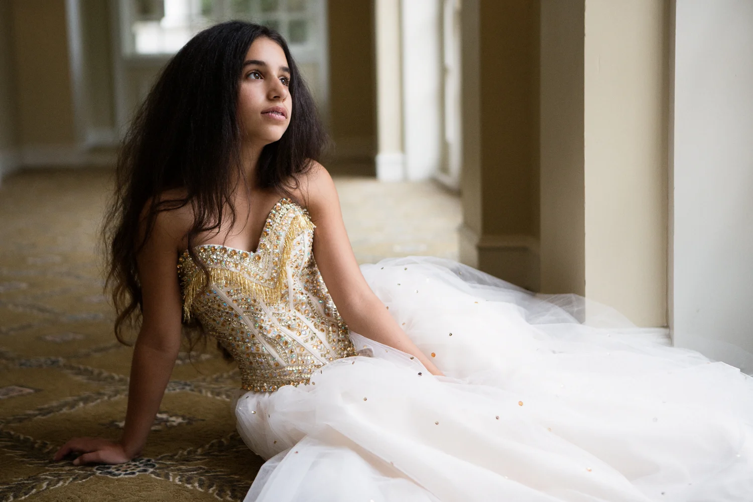 Portrait of bat mitzvah girl with long dark hair in gold and white strapless gown 