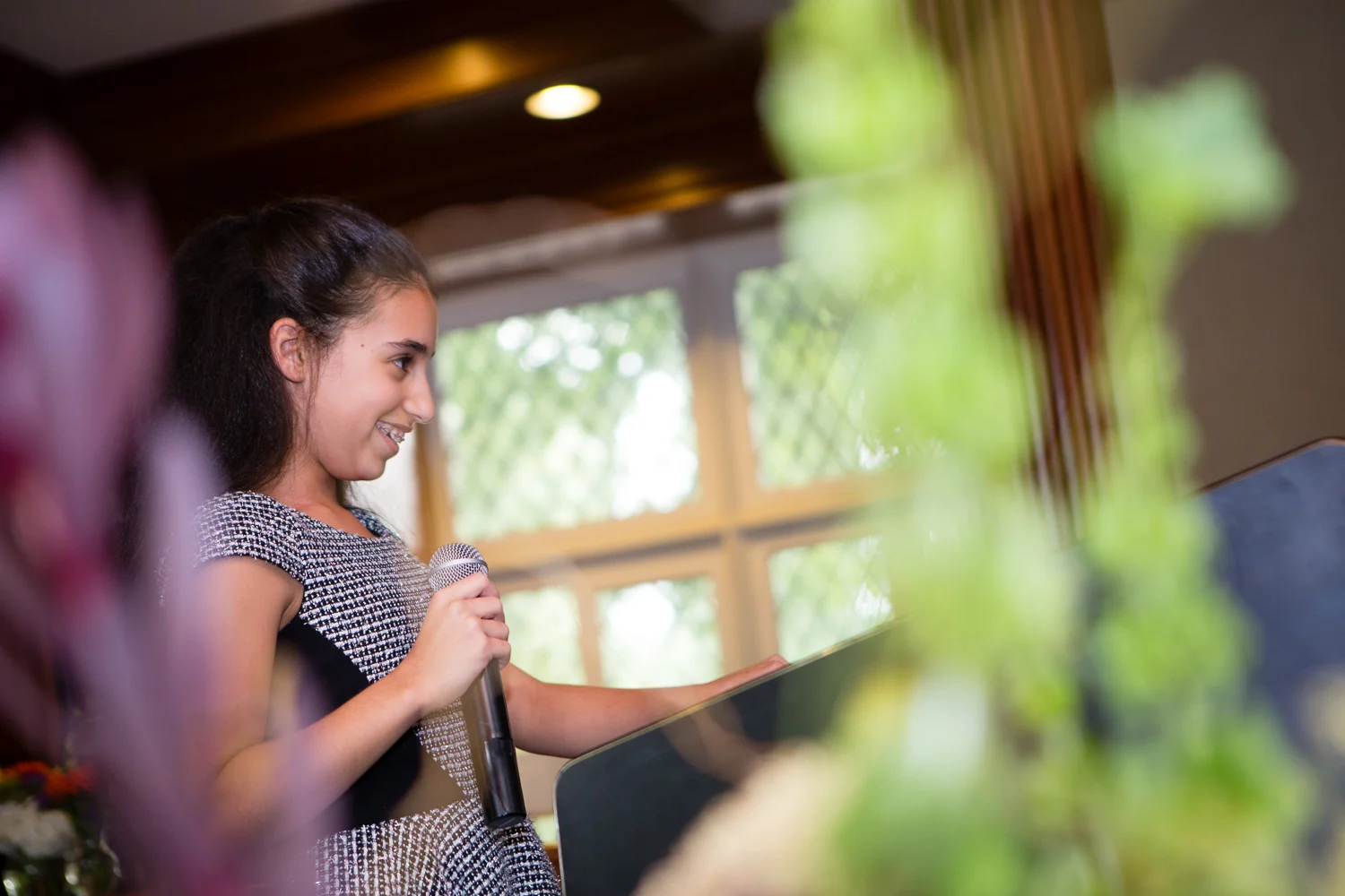 Photograph of bat mitzvah girl speaking into microphone and smiling during ceremony