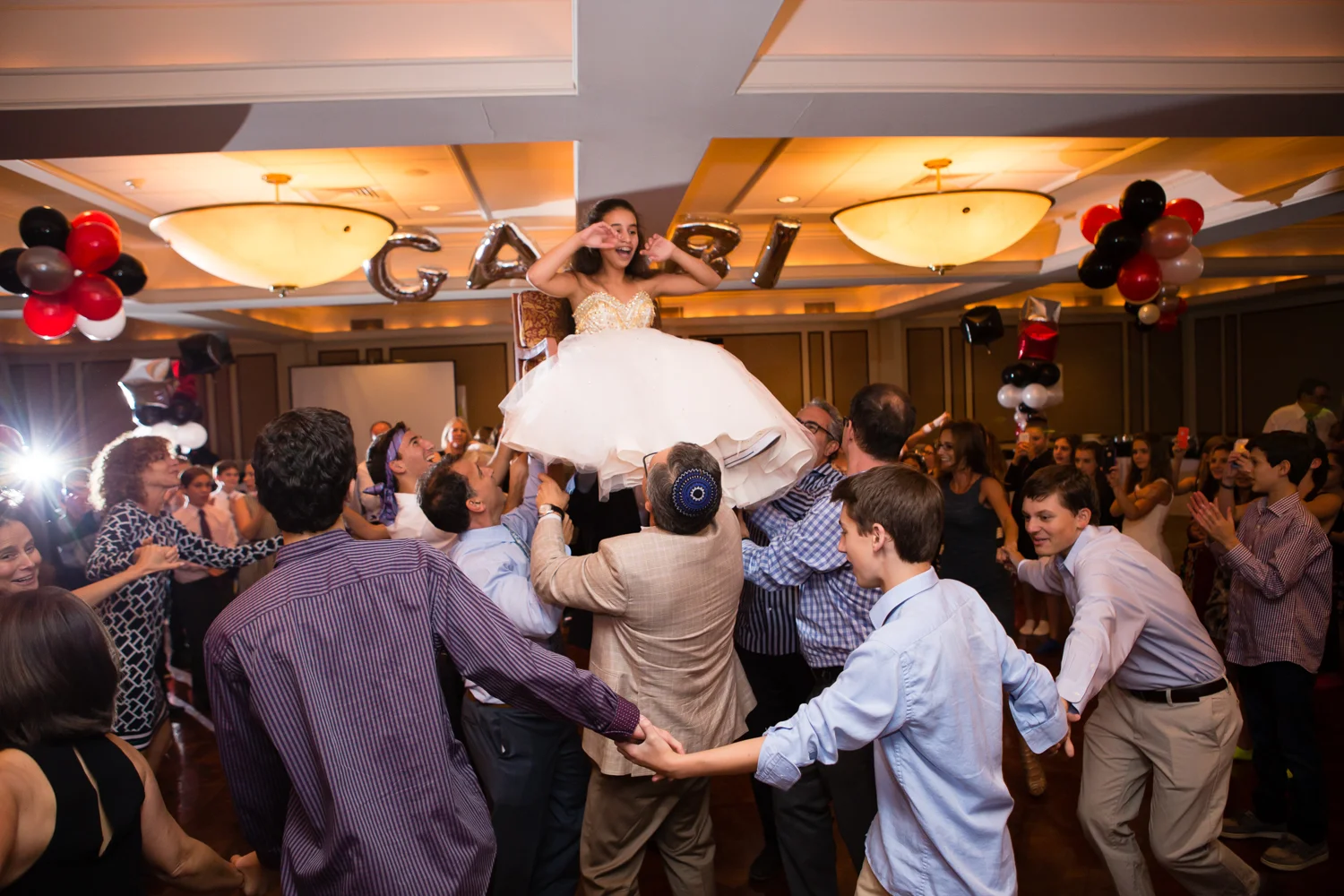 Photo of crowd dancing the hora and bat mitzvah girl on the chair