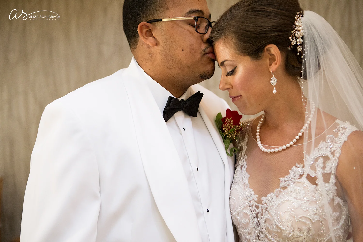 Photo of groom kissing his bride's forehead. Interracial couple.