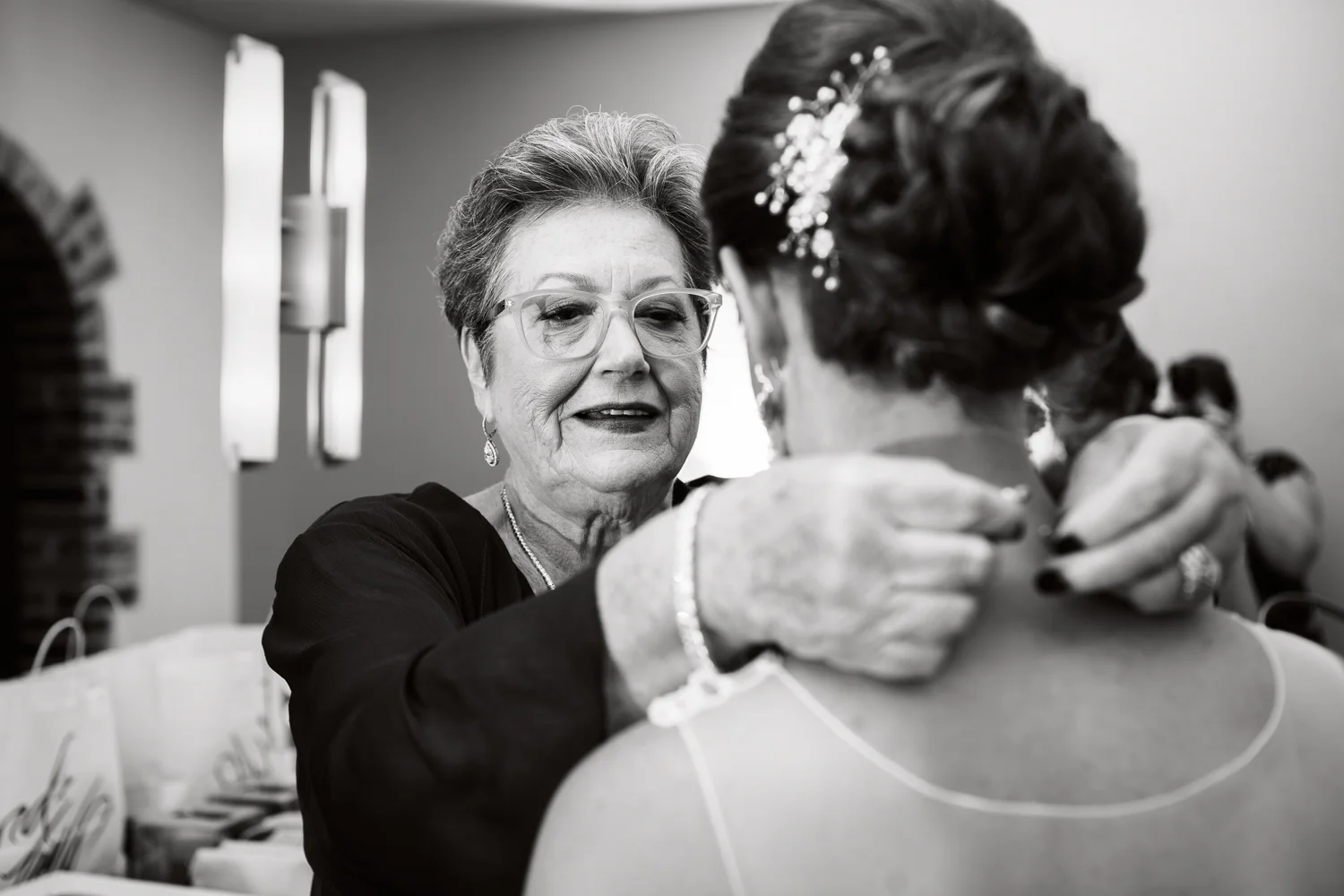 Black and white photo of mother putting necklace on her daughter, the bride.