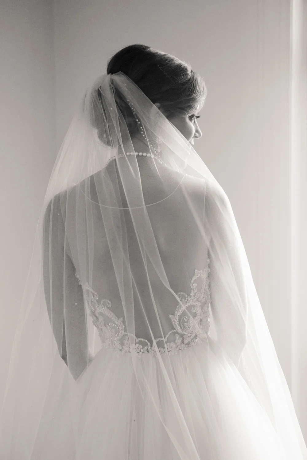 Black and white portrait of bride, back through sheer dress and veil