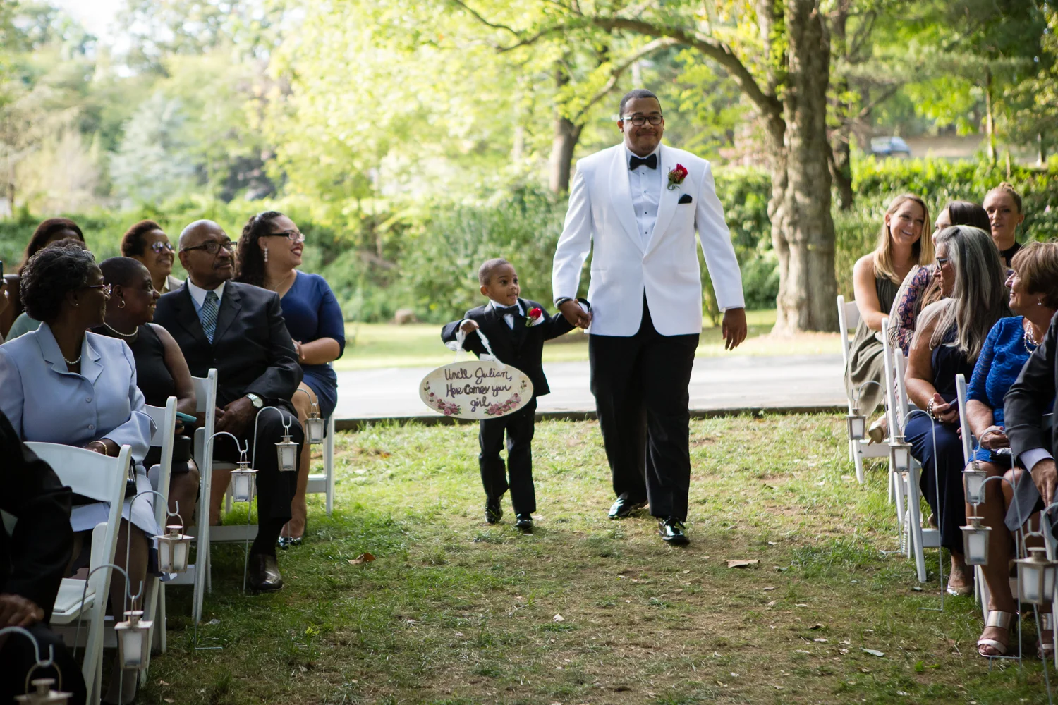 Photo of groom walking down aisle with the ring bearer at outdoor ceremony