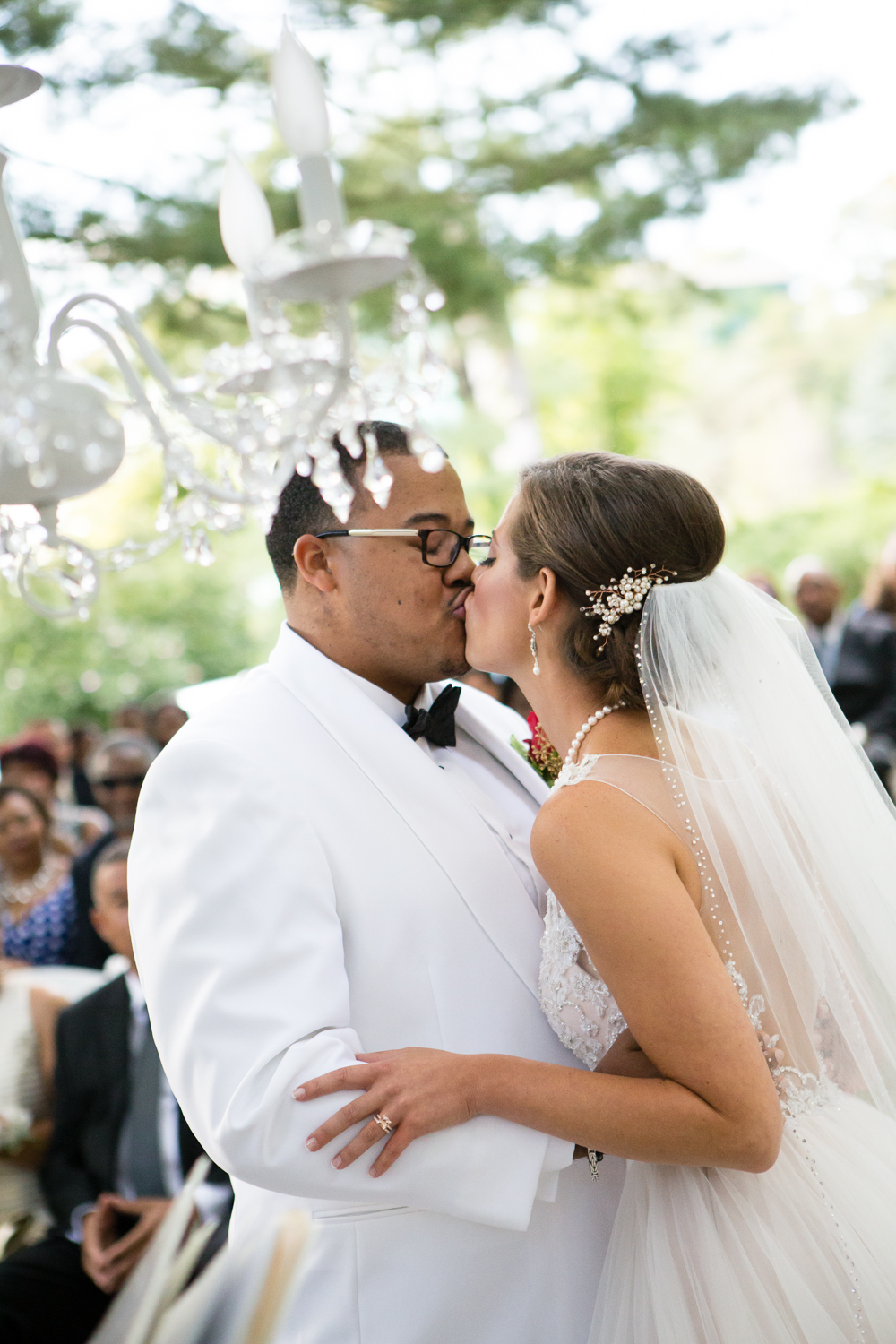 Photo of bride and groom kiss under chandelier in outdoor wedding ceremony