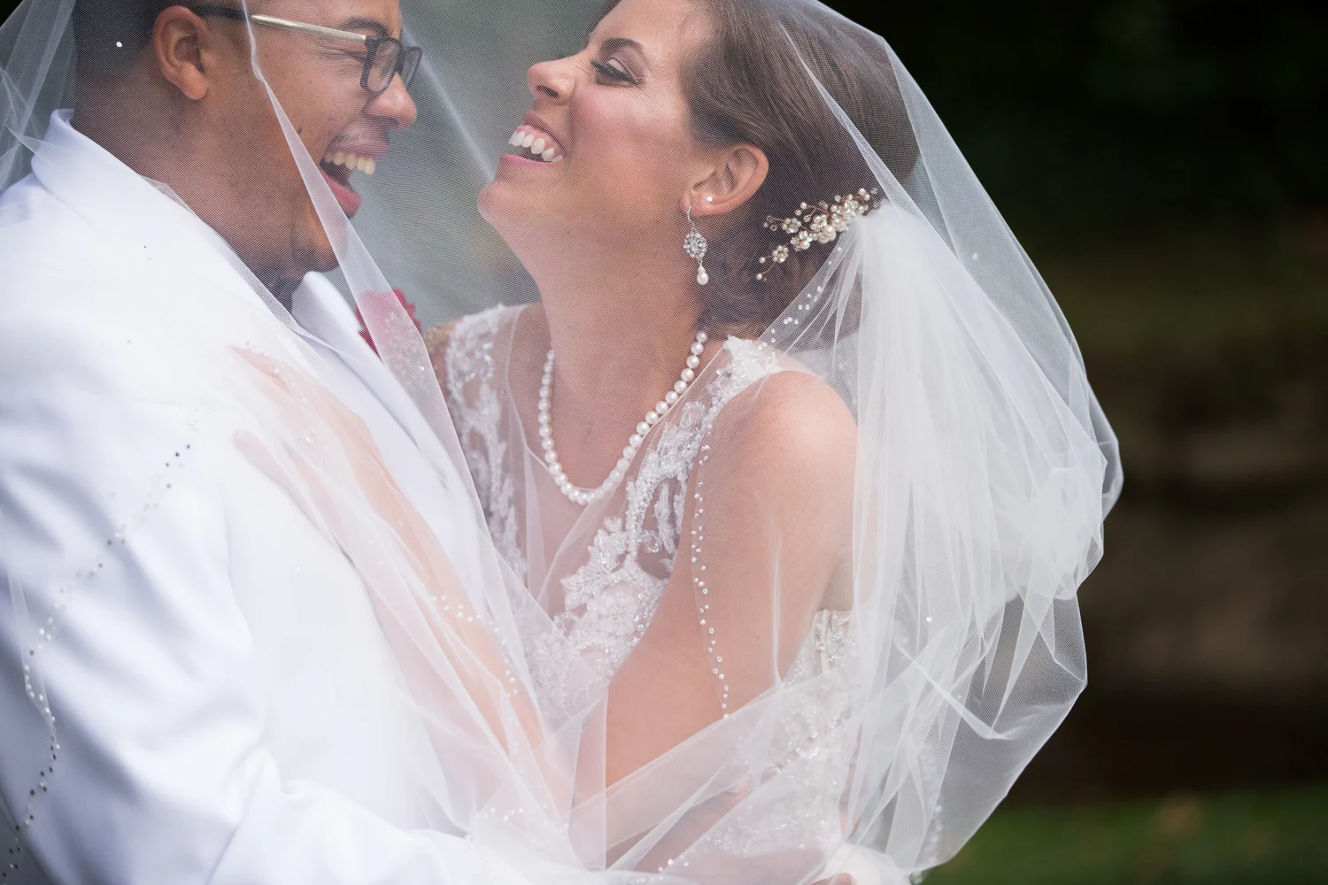 Portrait of bride and groom laughing under veil